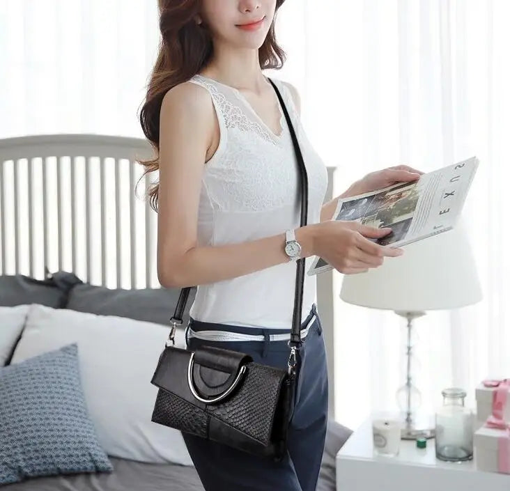 Donna con borsa a tracolla nera in pelle, design elegante, indossa top bianco e pantaloni blu, in una stanza moderna. Accessorio moda femminile.