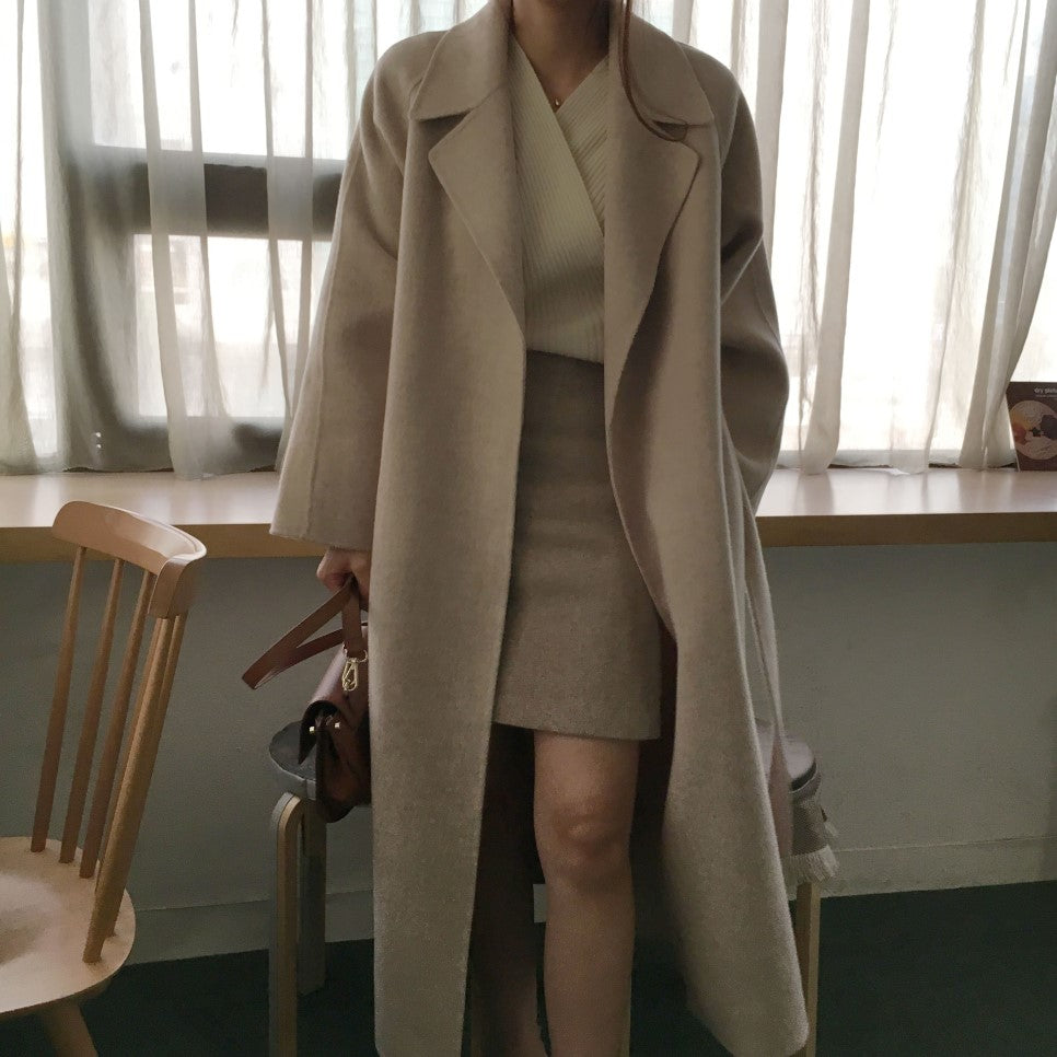 Donna con cappotto beige lungo, abito coordinato e borsa marrone. Moda autunnale elegante, abbigliamento casual chic, stile minimalista.