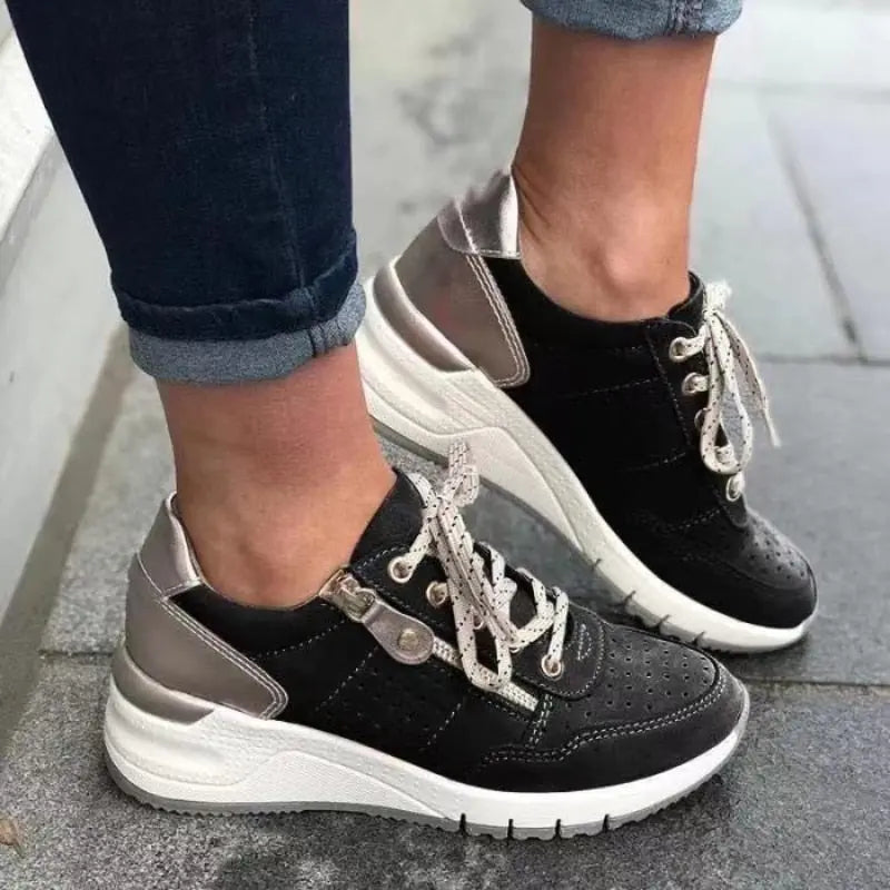 Scarpe da ginnastica nere e argento con lacci bianchi, indossate su pavimento grigio. Sneakers moda donna, comode e trendy.