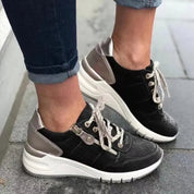 Scarpe da ginnastica nere e argento con lacci bianchi, indossate su pavimento grigio. Sneakers moda donna, comode e trendy.