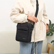 Borsa a tracolla nera unisex, design minimalista, indossata su giacca beige e jeans. Ideale per moda casual e praticità quotidiana.