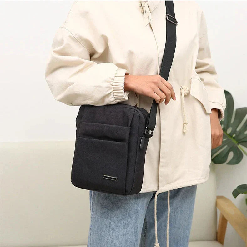 Borsa a tracolla nera unisex, design minimalista, indossata su giacca beige e jeans. Ideale per moda casual e praticità quotidiana.
