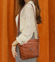 Borsa a tracolla in pelle marrone, indossata da una donna con camicia in pizzo bianco e gonna a quadri. Accessorio moda elegante e versatile.