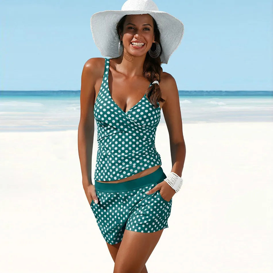 Donna sorridente in costume da bagno a pois verde con cappello bianco su spiaggia. Moda mare, abbigliamento estivo, vacanza al mare.