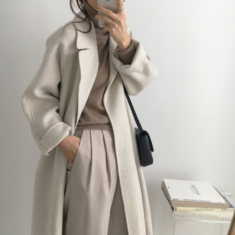 Donna con cappotto beige elegante, maglione marrone, pantaloni chiari e borsa nera. Moda autunnale minimalista, stile casual chic.