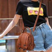 Borsa a tracolla in pelle marrone, design elegante e compatto, indossata con t-shirt nera e jeans. Accessorio moda donna, stile casual chic.