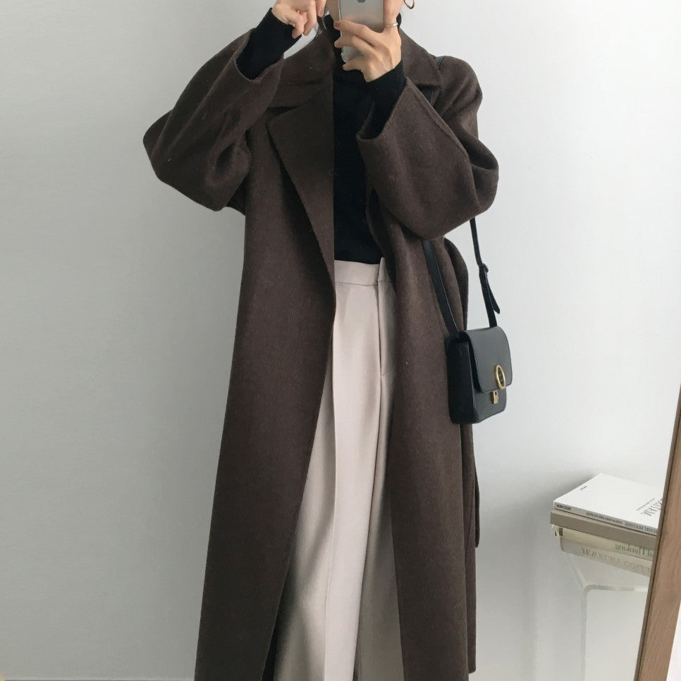 Cappotto lungo marrone elegante, abbinato a pantaloni chiari e borsa a tracolla nera. Moda autunnale donna, stile minimalista chic.