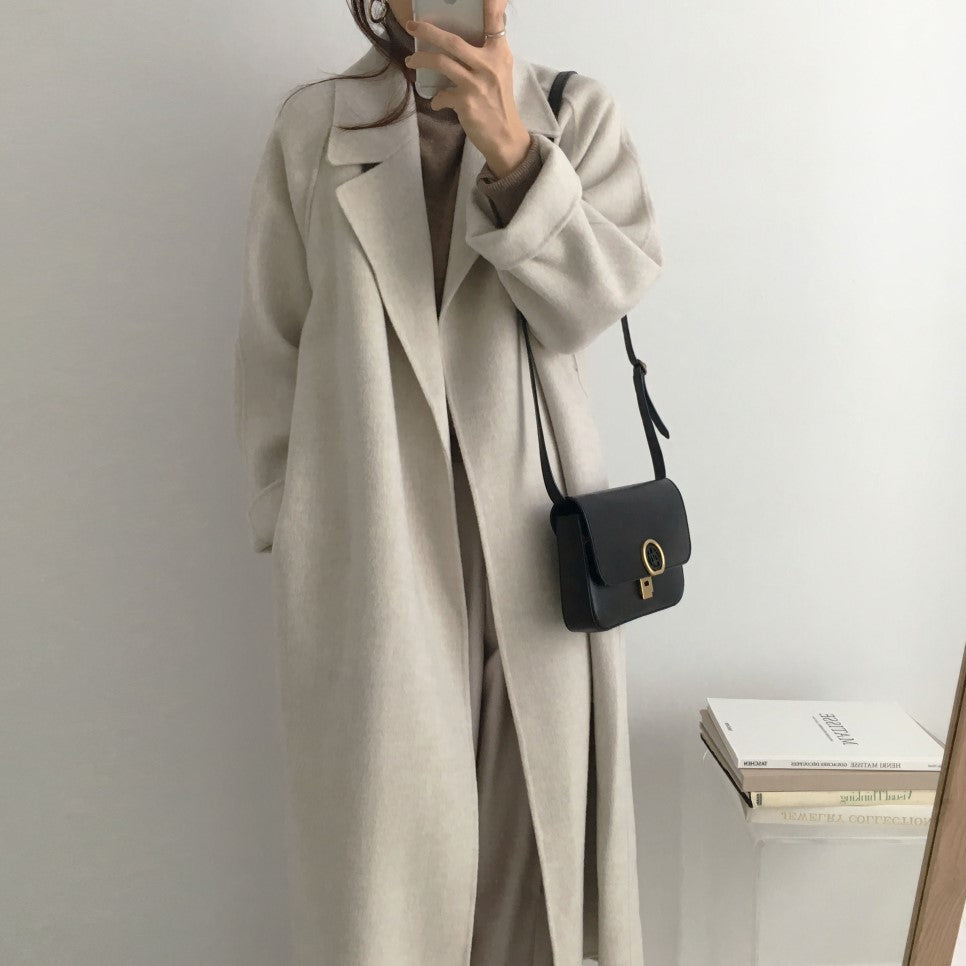Cappotto lungo beige elegante, donna, abbinato a borsa nera a tracolla. Moda autunnale minimalista, stile casual chic.