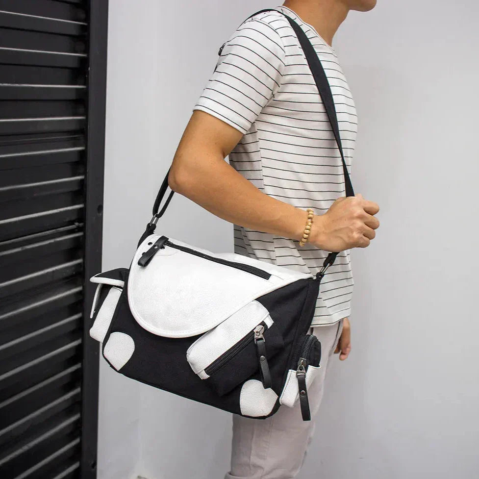 Borsa a tracolla uomo bianca e nera, design moderno, tasche multiple, indossata da persona con maglietta a righe. Accessorio moda casual.