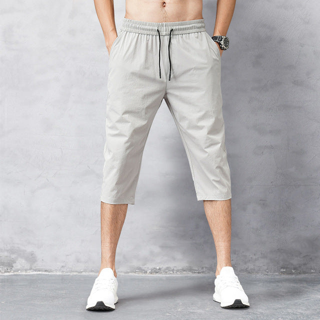Pantaloni sportivi da uomo grigi, lunghezza tre quarti, con coulisse in vita. Indossati con scarpe da ginnastica bianche.