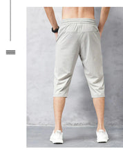 Pantaloni sportivi da uomo grigi, lunghezza tre quarti, indossati da modello di spalle. Design casual, elastico in vita, adatti per fitness e tempo libero.