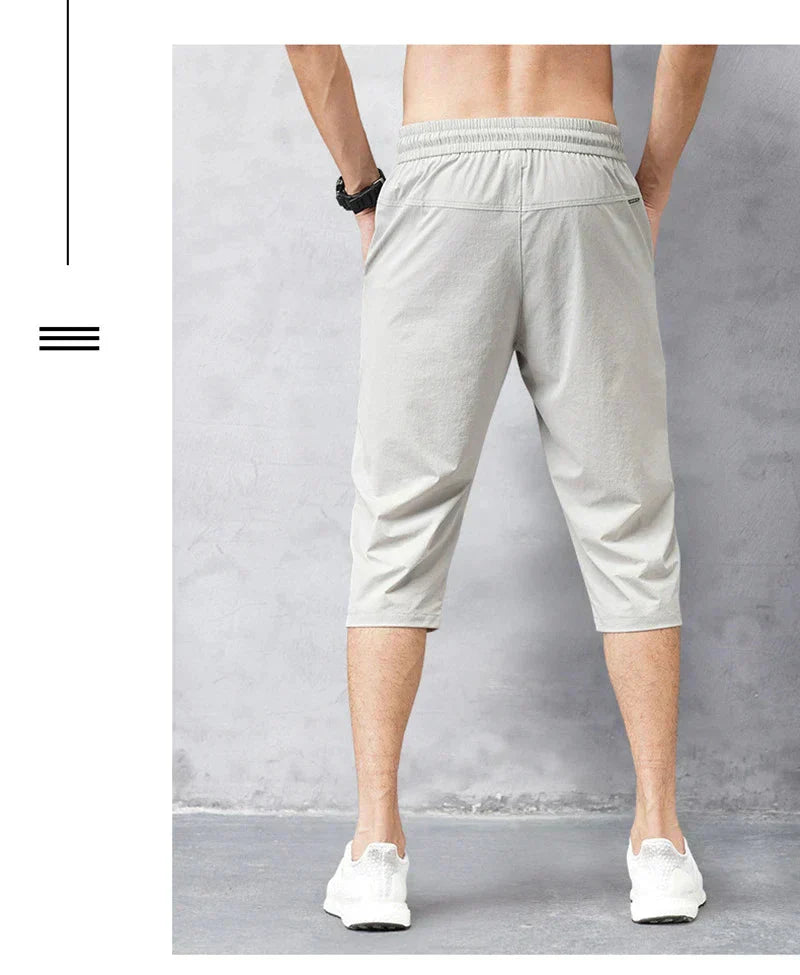 Pantaloni sportivi da uomo grigi, lunghezza tre quarti, indossati da modello di spalle. Design casual, elastico in vita, adatti per fitness e tempo libero.