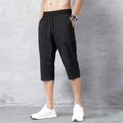 Pantaloni sportivi neri da uomo, lunghezza tre quarti, con elastico in vita e tasche laterali. Indossati con scarpe da ginnastica bianche.