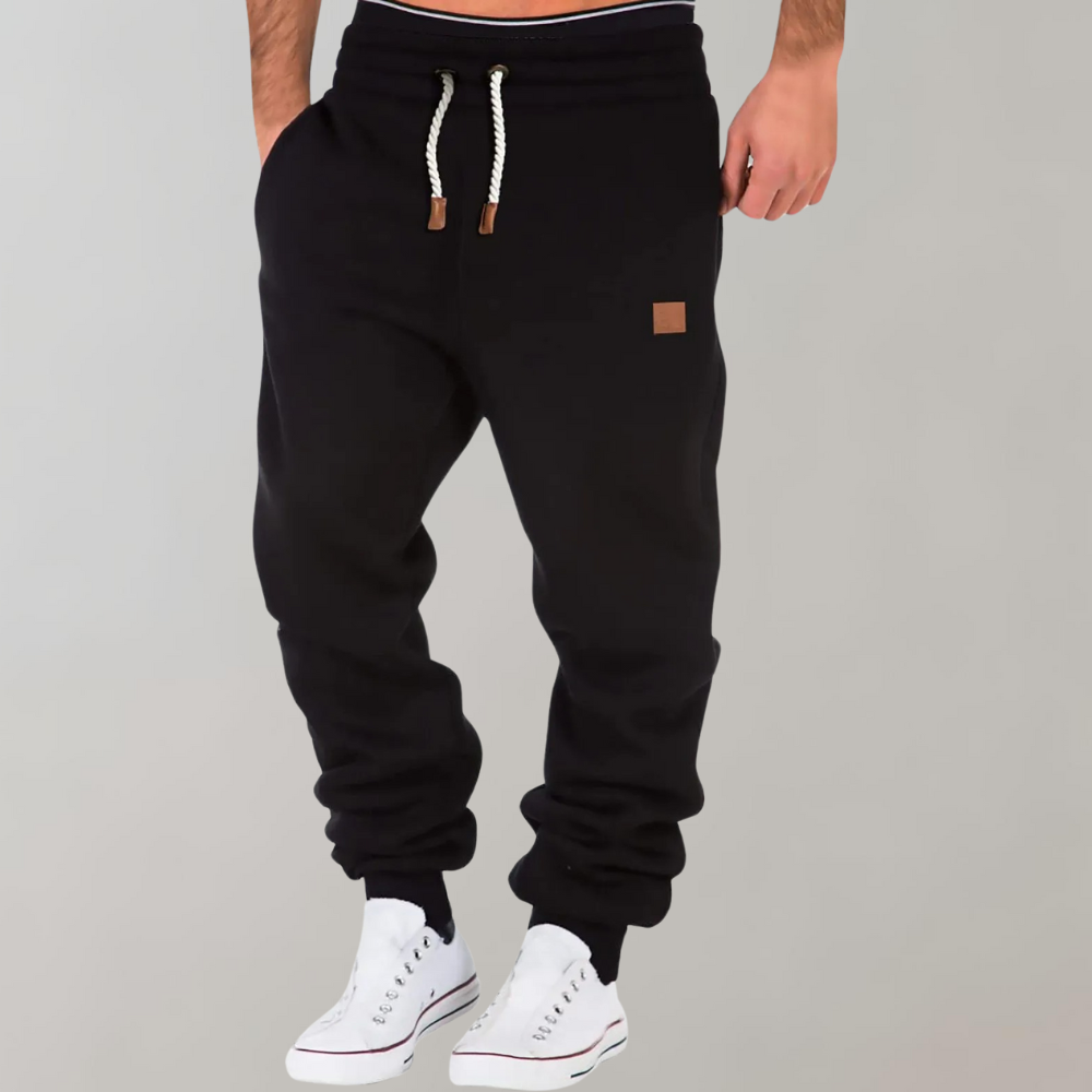 Pantaloni jogger neri da uomo con coulisse, tasca laterale, indossati con sneakers bianche. Stile casual, comodi per sport e tempo libero.