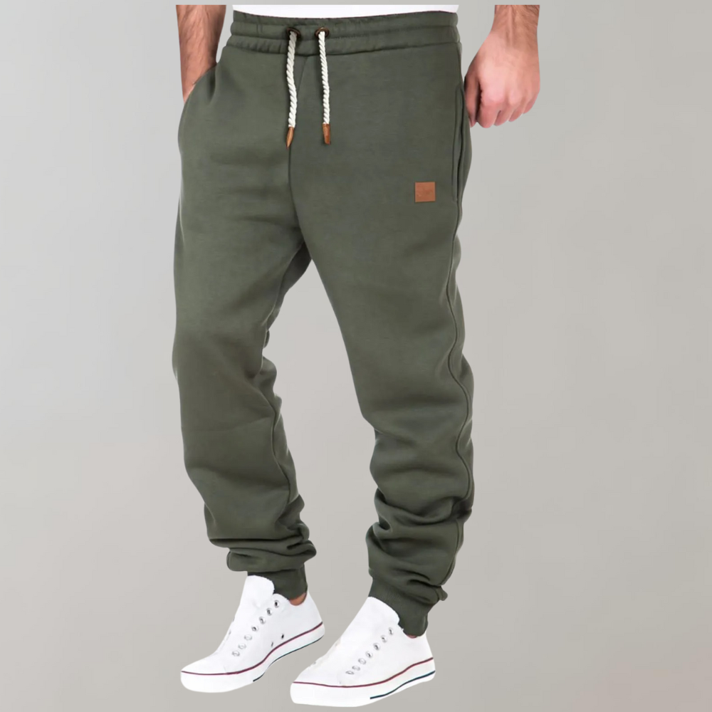 Pantaloni jogger verde oliva da uomo, con coulisse bianca e dettagli in pelle, abbinati a scarpe da ginnastica bianche. Moda casual maschile.