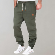 Pantaloni jogger verde oliva da uomo, con coulisse bianca e dettagli in pelle, abbinati a scarpe da ginnastica bianche. Moda casual maschile.