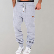 Pantaloni tuta grigi da uomo con coulisse, tasche laterali, polsini elasticizzati, abbinati a scarpe da ginnastica bianche.