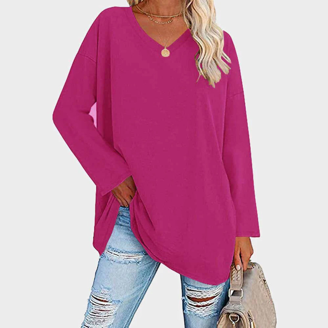Maglia oversize fucsia da donna con scollo a V, abbinata a jeans strappati e borsa beige. Look casual e alla moda per l'autunno.