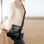 Borsa a tracolla nera in pelle, indossata da una donna con maglia bianca in pizzo. Accessorio moda elegante, perfetto per look casual e chic.
