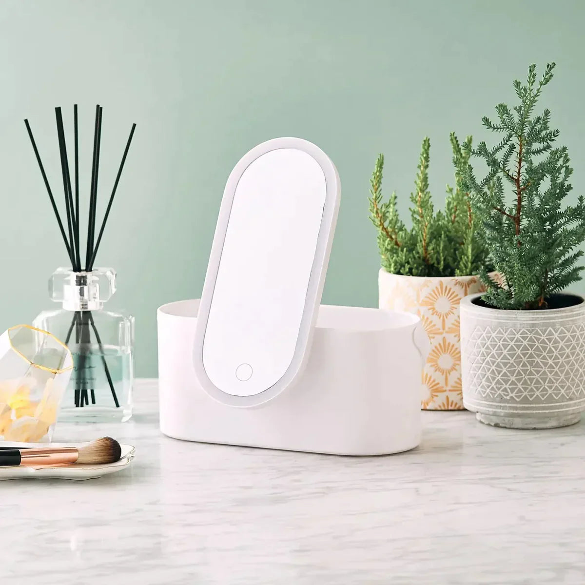 Sterilizzatore UV bianco su tavolo di marmo, circondato da piante in vaso e diffusore di aromi. Design moderno, ideale per igienizzare smartphone e accessori.