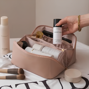 Beauty case rosa con prodotti cosmetici, tra cui profumo Byredo Desert Soul, pennelli trucco e flaconi skincare. Accessori eleganti per routine di bellezza.