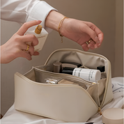 Astuccio cosmetico beige aperto con prodotti di bellezza, flaconi e creme. Mani femminili applicano siero. Accessori eleganti, cura della pelle.