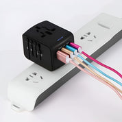 Adattatore universale da viaggio nero con porte USB multiple, collegato a una presa multipla bianca. Cavi colorati connessi. Accessorio elettronico versatile.
