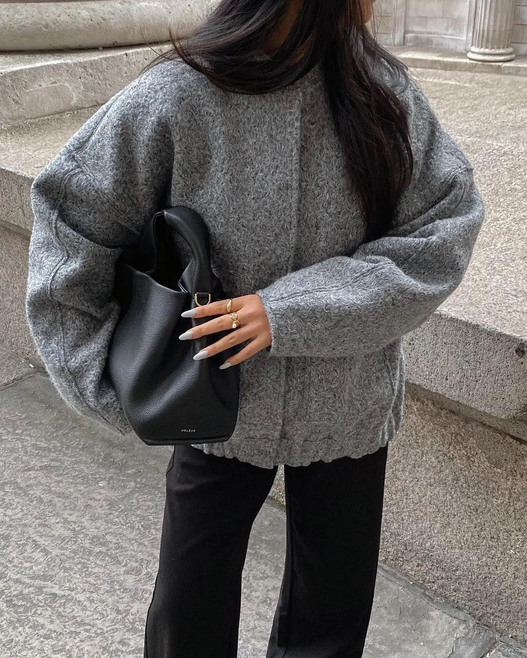 Donna con maglione grigio oversize e borsa nera in pelle, moda autunnale elegante, look casual chic, abbigliamento invernale caldo e confortevole.