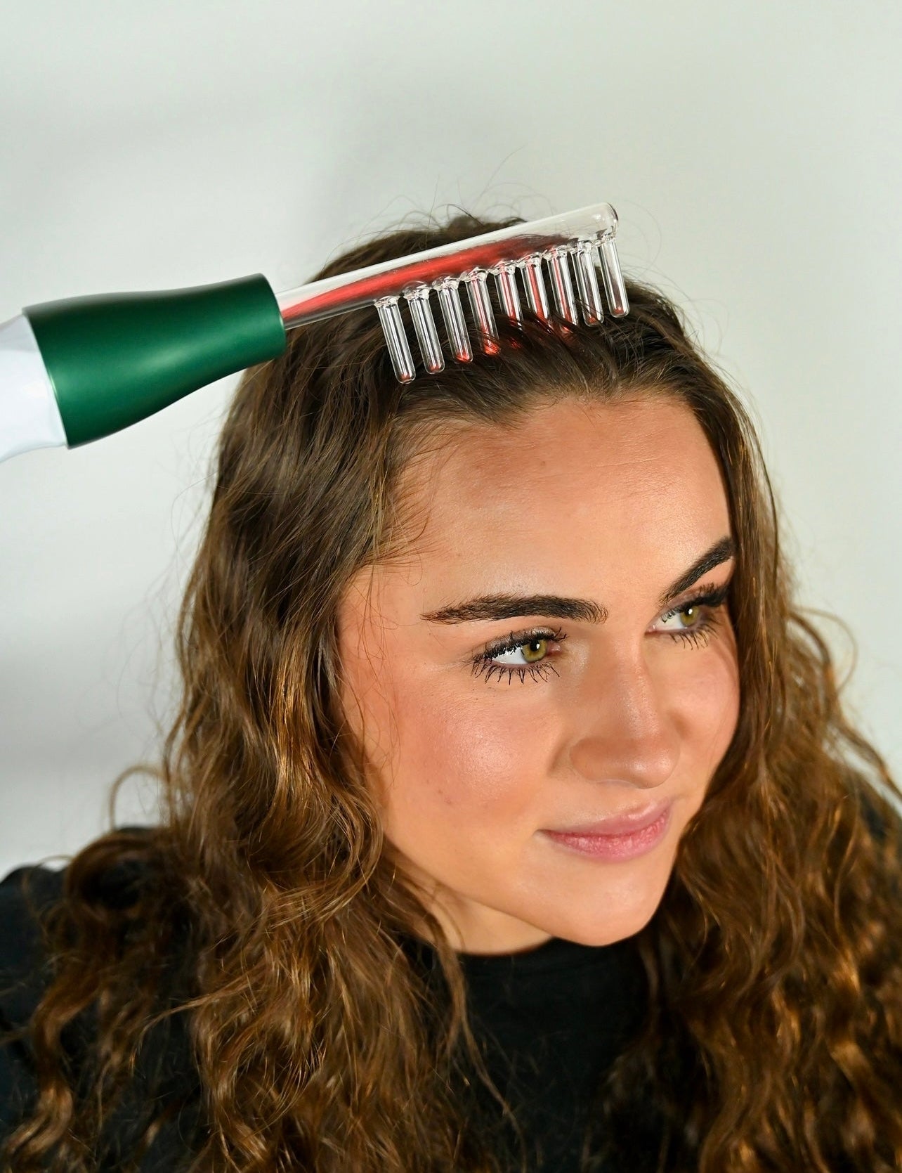 Donna utilizza pettine laser per capelli su sfondo bianco. Trattamento crescita capelli, stimolazione cuoio capelluto, cura capelli.