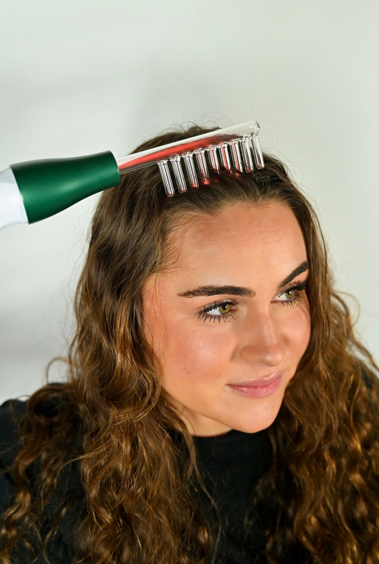 Donna utilizza pettine laser per capelli su sfondo bianco. Trattamento crescita capelli, stimolazione cuoio capelluto, cura capelli.