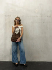 Donna con occhiali indossa jeans a zampa e top bianco, tiene borsa a spalla marrone. Moda casual, stile urbano, abbigliamento femminile trendy.