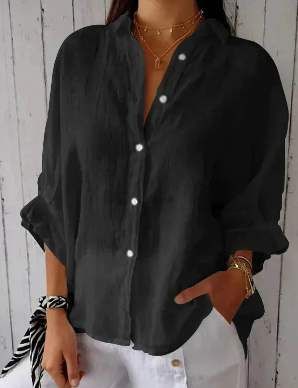 Camicia nera da donna in lino, maniche lunghe, bottoni bianchi, stile casual, abbinata a pantaloni bianchi. Accessori: bracciali e collana dorati.