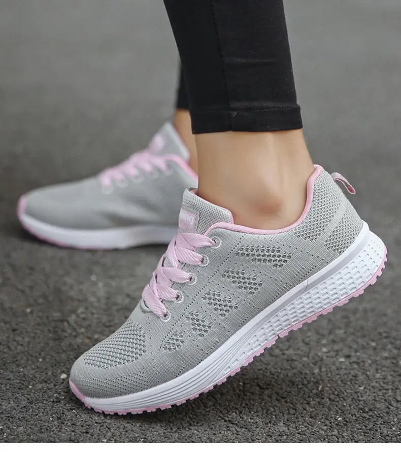 Scarpe da ginnastica grigie da donna con lacci rosa, suola bianca antiscivolo, design traspirante, ideali per corsa e fitness su strada asfaltata.