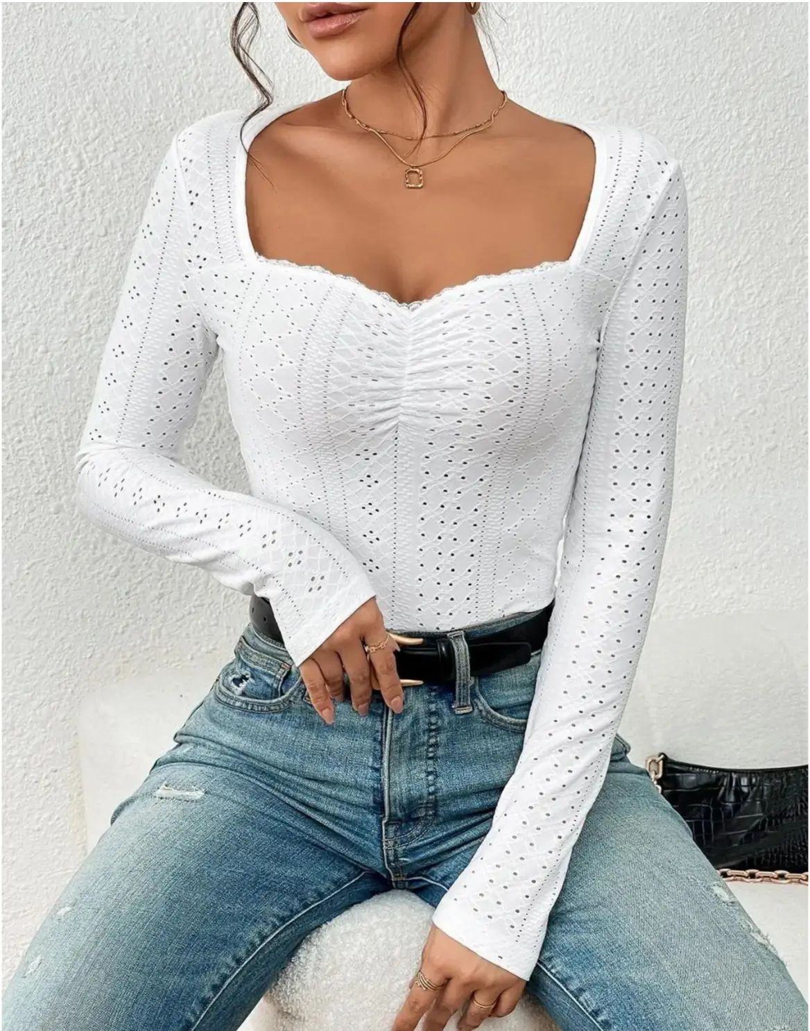 Donna con top bianco a maniche lunghe traforato, scollo quadrato, abbinato a jeans blu. Look casual elegante, moda femminile autunno.