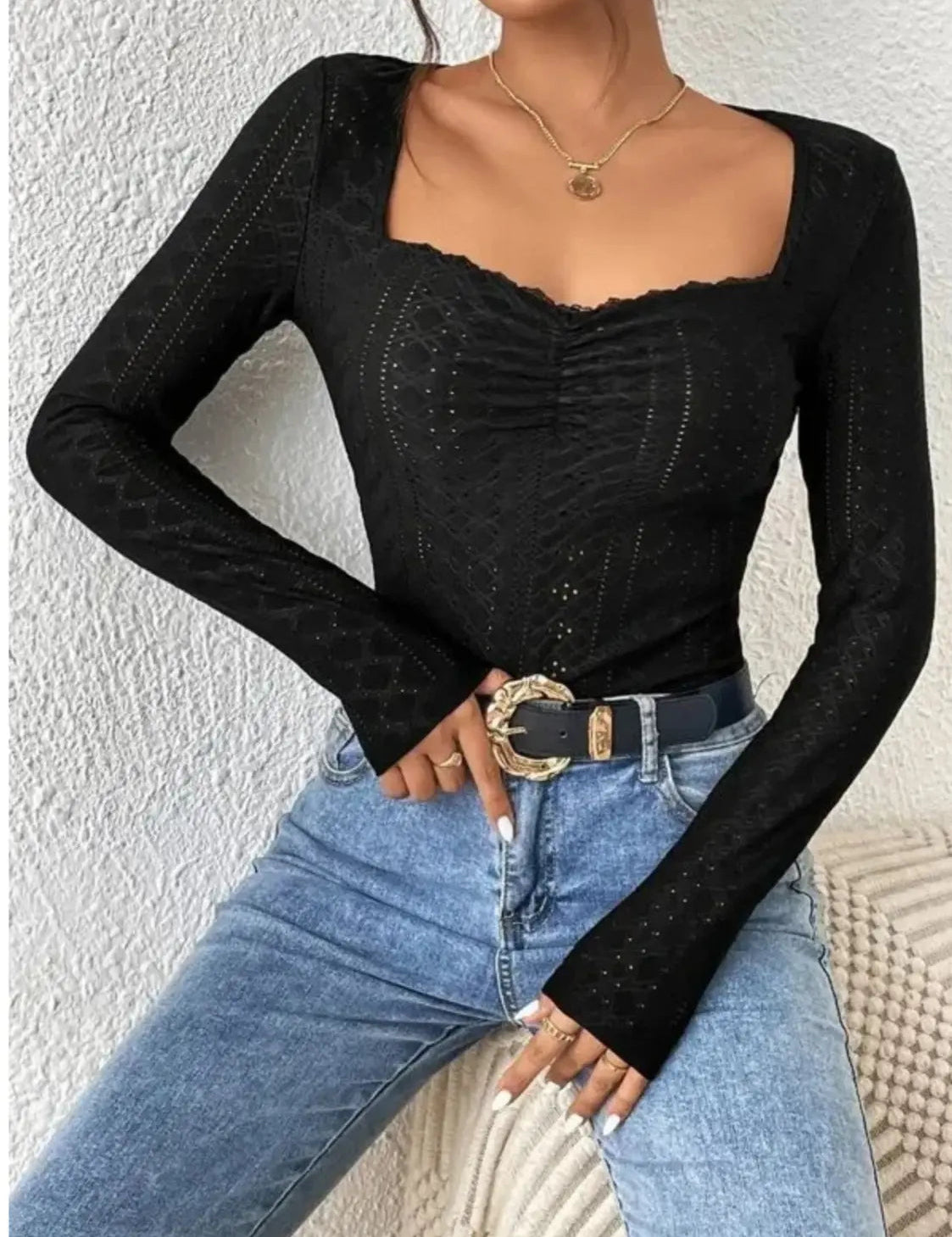 Donna con top nero a maniche lunghe e jeans blu, cintura con fibbia dorata. Moda casual elegante, abbigliamento femminile trendy.