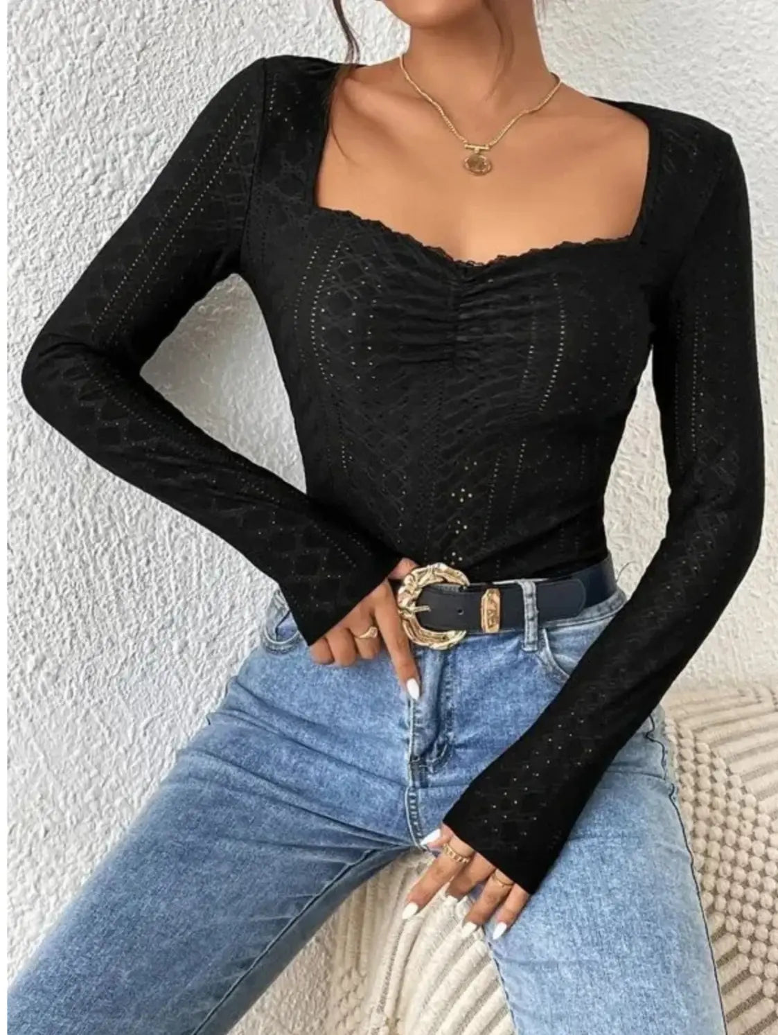 Donna con top nero a maniche lunghe e jeans blu, cintura con fibbia dorata. Moda casual elegante, abbigliamento femminile trendy.