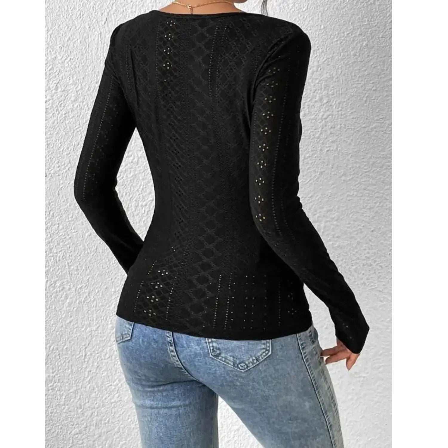 Maglia nera a maniche lunghe in pizzo traforato, indossata con jeans blu. Design elegante e moderno, ideale per look casual e sofisticati.
