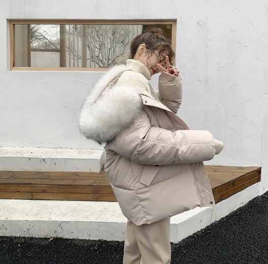 Giacca invernale beige con cappuccio in pelliccia sintetica bianca, indossata da una donna all'aperto. Moda invernale, abbigliamento caldo ed elegante.