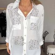 Camicia bianca da donna con scritte nere, maniche lunghe, colletto classico e tasca frontale. Elegante e casual, perfetta per ogni occasione.