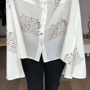 Camicia bianca trasparente con scritte nere, maniche ampie, abbottonatura frontale, stile elegante e moderno, perfetta per moda femminile casual.
