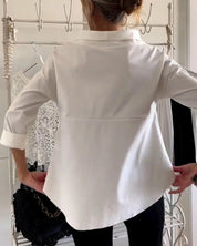 Camicia bianca elegante da donna, maniche lunghe, indossata da una persona di spalle. Sfondo con abiti appesi. Moda femminile, abbigliamento casual.