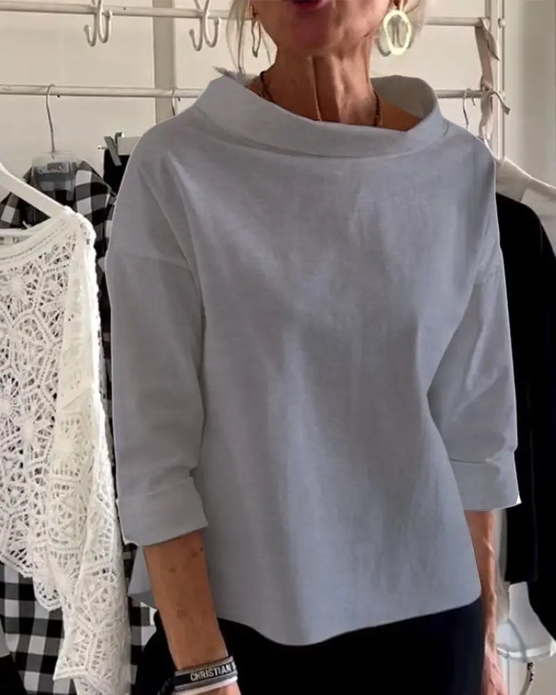 Donna indossa maglia grigia a maniche lunghe, con abbigliamento appeso sullo sfondo. Moda casual elegante, stile minimalista.