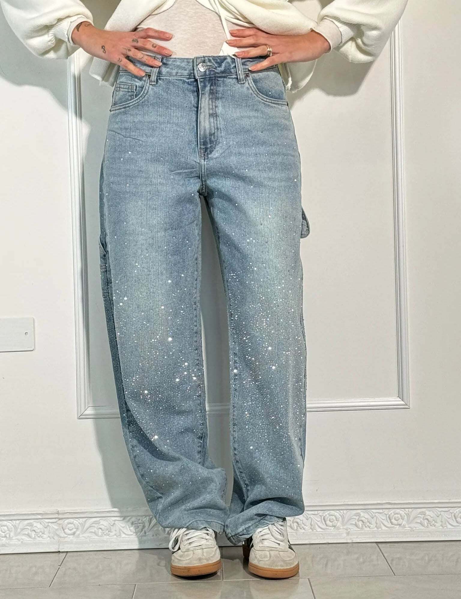 Jeans a gamba larga in denim chiaro con dettagli glitterati, indossati con sneakers bianche. Moda casual, stile trendy, abbigliamento femminile.