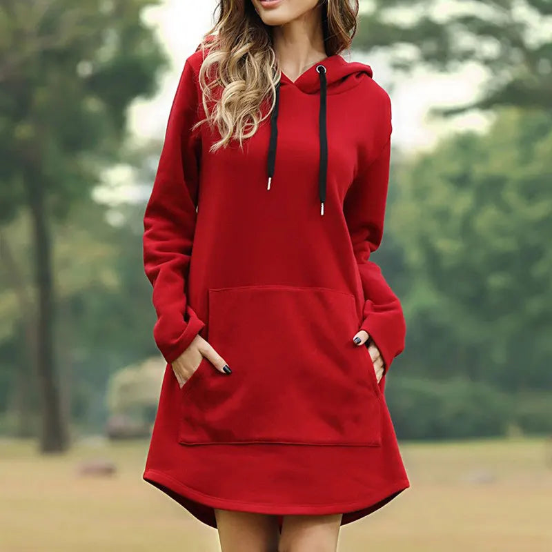 Donna con felpa rossa con cappuccio, tasche frontali, in un parco verde. Abbigliamento casual autunnale, moda femminile, stile confortevole.