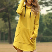 Donna con felpa gialla con cappuccio, tasca frontale e lacci neri, in un parco. Moda casual autunnale, abbigliamento comodo e trendy.