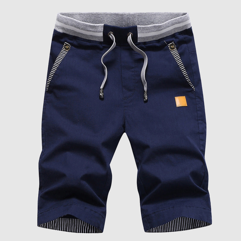 Pantaloncini uomo blu scuro con coulisse, tasche con zip, dettagli a righe, cintura elastica grigia. Moda estiva casual, abbigliamento maschile.