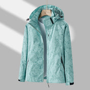 Giacca impermeabile donna verde menta con cappuccio, motivo foglie, chiusura zip, tasche laterali, ideale per escursioni e attività outdoor.