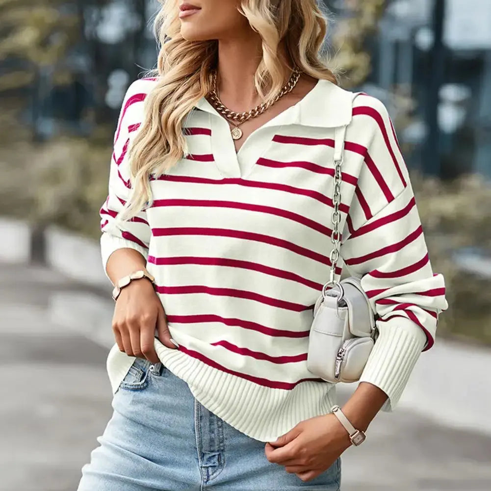 Donna con maglione a righe bianche e rosse, jeans chiari, borsa a tracolla bianca, collana dorata. Moda casual autunnale, look urbano elegante.