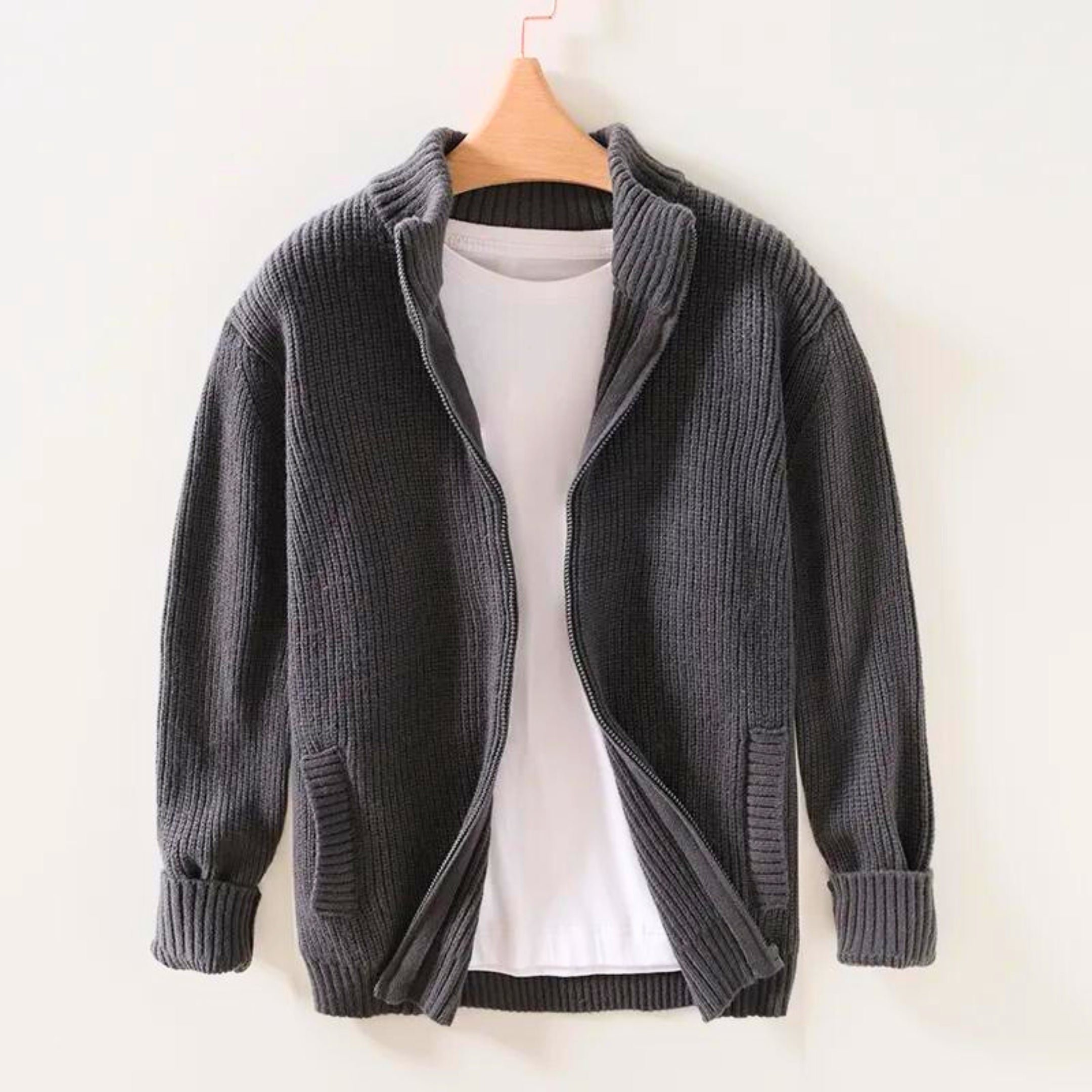 Giacca cardigan in maglia grigia con zip, appesa su gruccia, sopra maglietta bianca. Moda uomo, abbigliamento casual, stile autunnale.