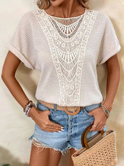 Donna con maglia bianca traforata e dettagli in pizzo, shorts di jeans, cintura marrone e borsa di paglia. Look estivo casual chic.